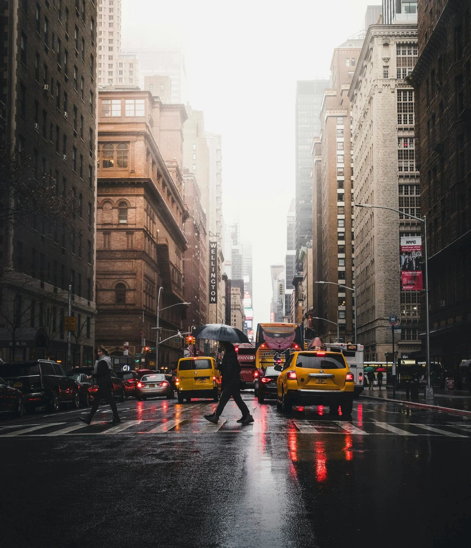 A rainy Manhattan avenue seen down the block, taxis and pedestrians at street level.